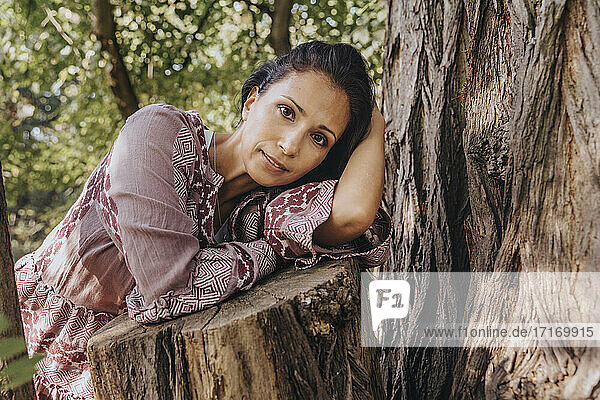 Mature woman staring while resting on tree trunk at park