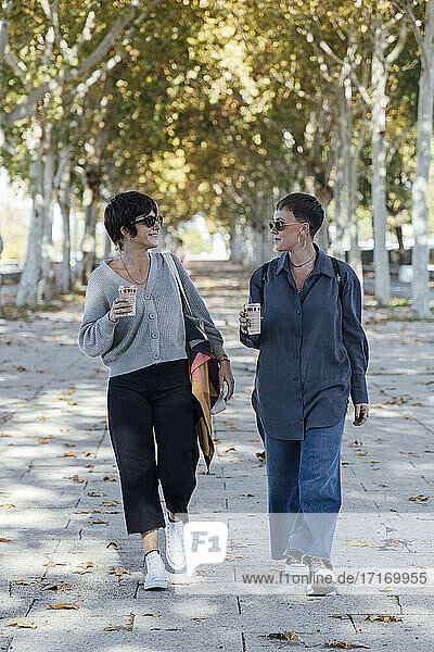Junge Frauen mit Kaffeetasse im Gespräch auf dem Fußweg