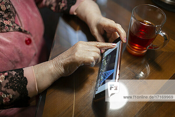 Ältere Frau berührt den Bildschirm des Mobiltelefons auf dem Tisch zu Hause