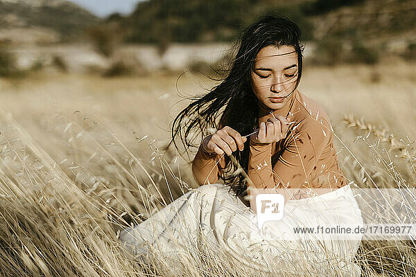 Young woman contemplating while sitting amidst gfrass in field during windy day
