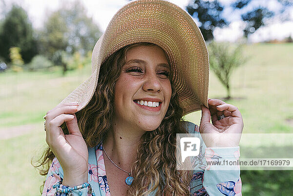 Smiling young woman wearing sun hat at public park during sunny day