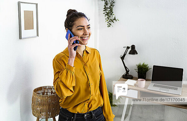 Young woman smiling while talking on mobile phone standing at home