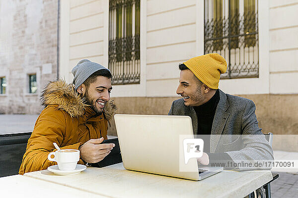 Homosexuell Männer lächelnd bei der Verwendung von digitalen Tablet und Laptop sitzen auf dem Bürgersteig Cafe