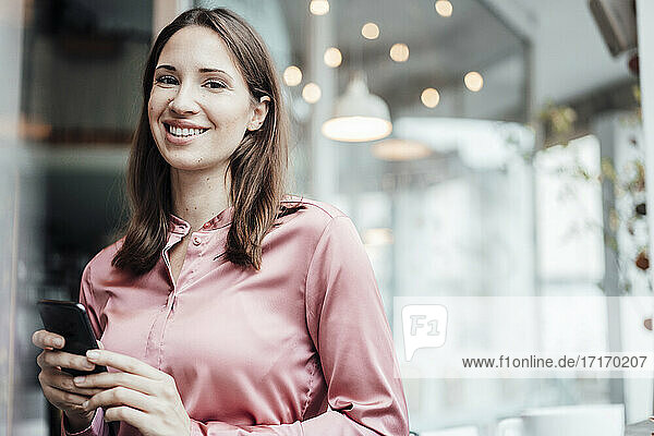 Lächelnde weibliche Fachkraft mit Mobiltelefon in einem Cafe