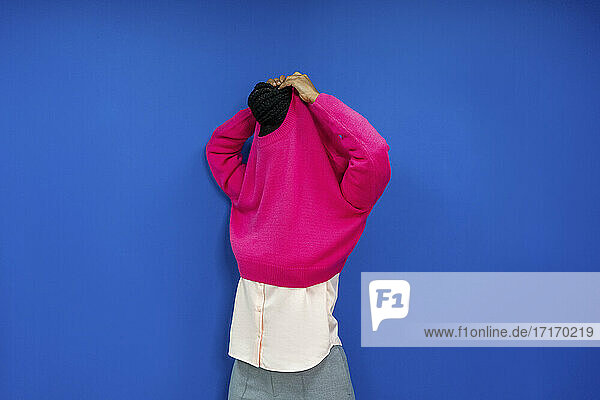 Weiblicher Unternehmer  der sein Sweatshirt auszieht  während er an einer blauen Wand am Arbeitsplatz steht