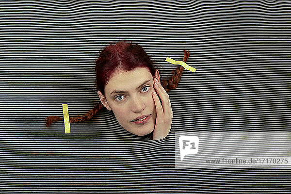 Studio shot of head of young woman wearing pigtails sticking out of gray striped background