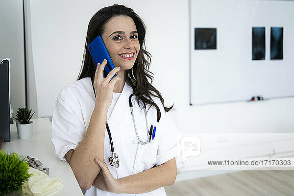 Lächelnde Ärztin  die in einer Klinik mit einem Mobiltelefon spricht