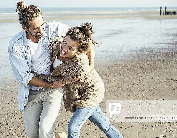 Fröhliches junges Paar  das am Wochenende am Strand spazieren geht und sich umarmt