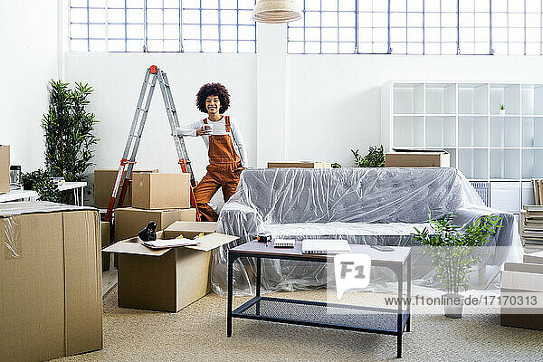 Afro-Frau  die eine Kaffeetasse hält  während sie auf einer Leiter in einem neuen Haus steht