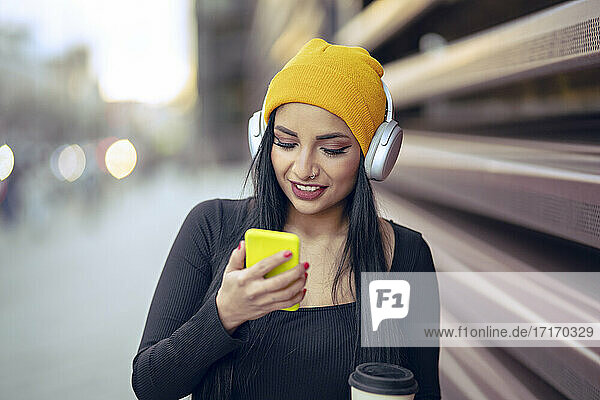 Young beautiful woman listening music over headphones while using smart phone at street