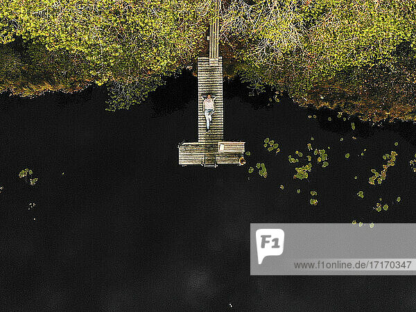 Luftaufnahme einer Frau  die auf einem Steg über einem See im Wald liegt