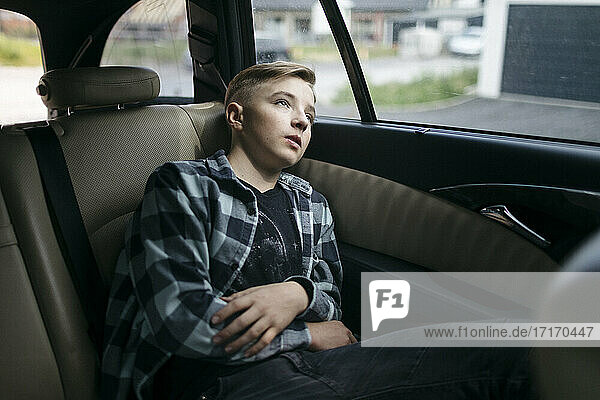 Thoughtful boy looking through window while sitting in back seat of car