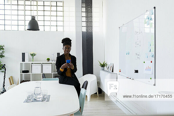 Young Afro businesswoman using smart phone while sitting on desk at office