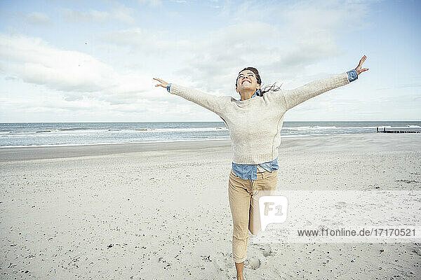 Porträt einer jungen Frau  die mit erhobenen Armen am Sandstrand läuft