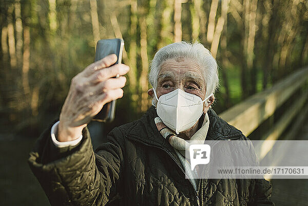Ältere Frau trägt Schutzmaske  während sie ein Selfie mit ihrem Smartphone im Winter macht
