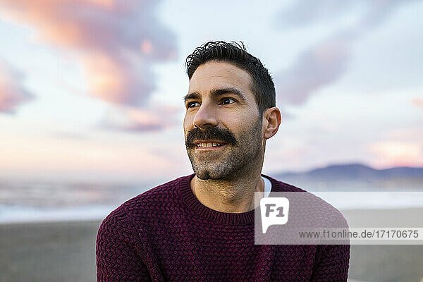 Handsome man in maroon sweater day dreaming at beach during sunrise