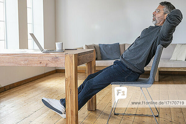 Geschäftsmann ruht sich aus  während er mit den Händen hinter dem Kopf im Büro zu Hause sitzt