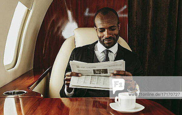 Junger Geschäftsmann liest Zeitung während einer Reise im Flugzeug