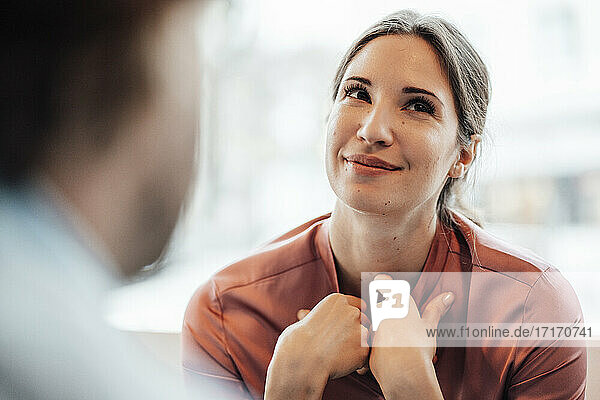 Lächelnde Geschäftsfrau schaut weg  während sie mit einem männlichen Kollegen in einem Café diskutiert