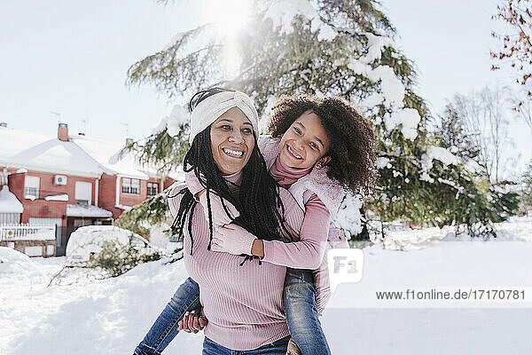Mother looking away while giving piggyback ride to daughter on snow covered land
