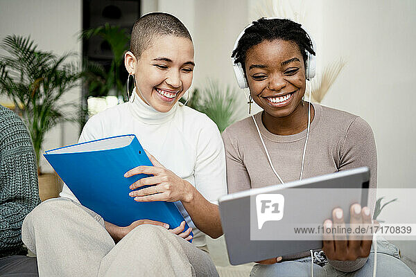 Smiling businesswoman using digital tablet sitting by female colleague at home