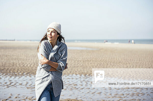 Young woman in cardigan sweater contemplating while walking on beach