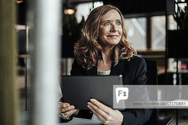 Nachdenkliche Geschäftsfrau mit digitalem Tablet  die im Büro wegschaut
