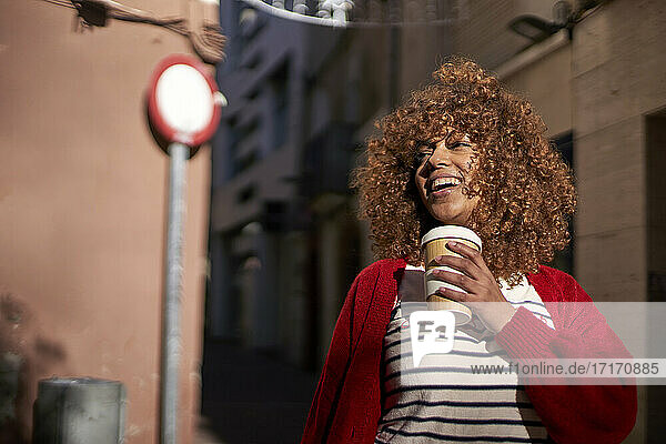 Smiling woman with disposable coffee cup looking away while standing outdoors