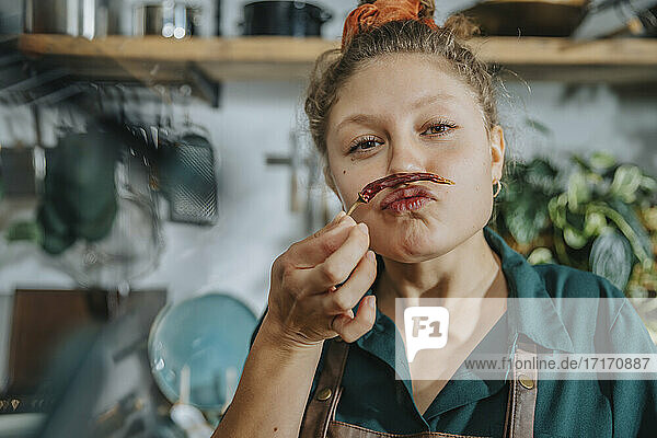 Playful chef making mustache with dry chili pepper while standing in kitchen