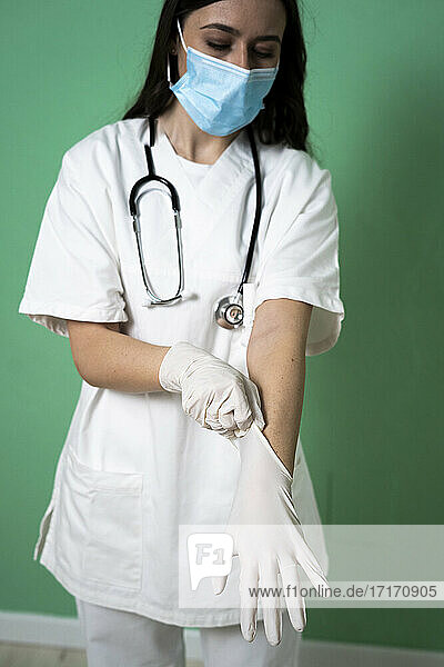 Junge Frau trägt Handschuh  während sie in einer Klinik an der Wand steht