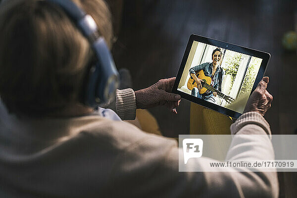 Junge Frau spielt Gitarre für ältere Frau bei Videoanruf über digitales Tablet zu Hause