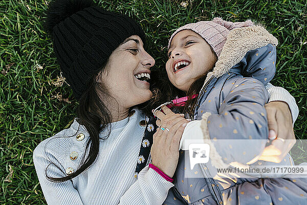 Smiling mother wearing knit hat playing with daughter while lying on grass