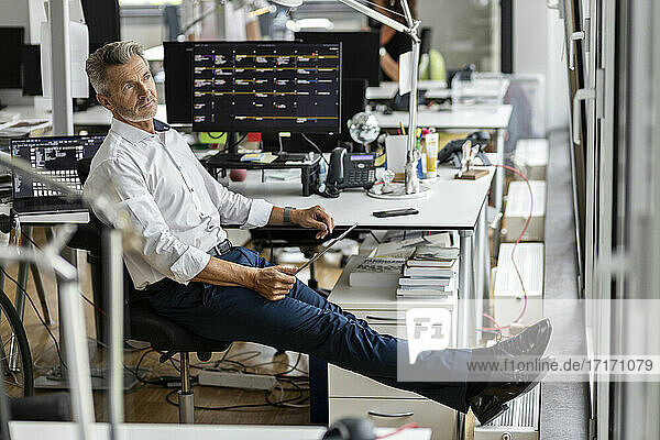 Nachdenklicher Unternehmer mit digitalem Tablet  der wegschaut  während er im Büro sitzt