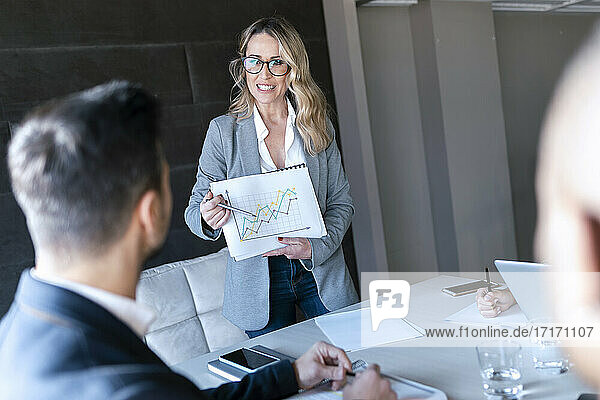 Smiling businesswoman showing graph while standing in office