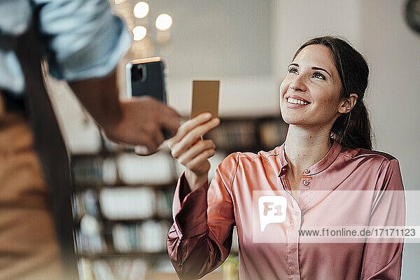 Glückliche weibliche Kundin  die mit Kreditkarte an einen männlichen Kellner in einem Café zahlt