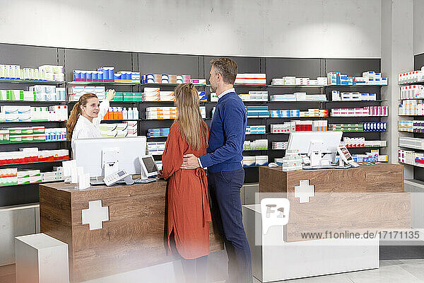 Couple standing at checkout while talking to female pharmacist