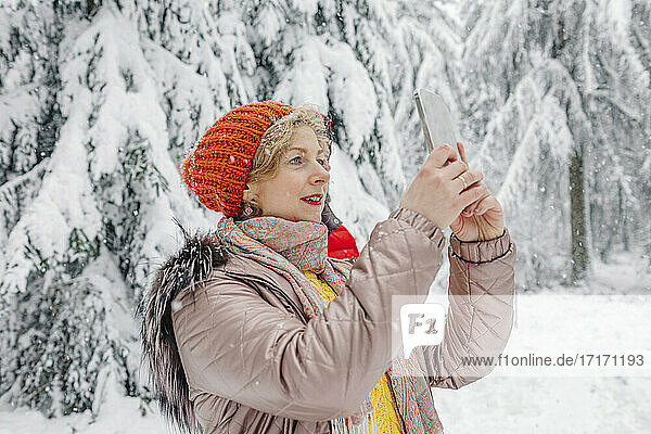 Mature woman wearing warm clothing using mobile phone while standing in forest