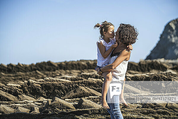 Mother kissing daughter while standing on flysch against blue sky