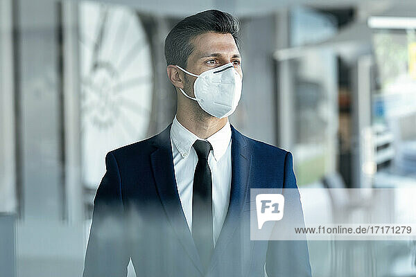 Geschäftsmann mit Gesichtsschutzmaske  der wegschaut  während er im Büro steht