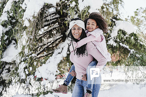 Happy mother giving piggyback ride to daughter in park