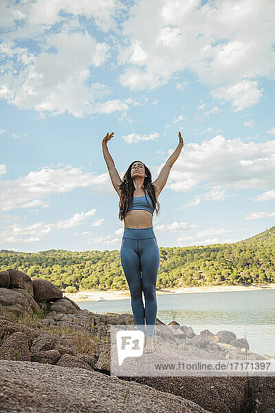 Frau übt Yoga mit erhobenen Armen auf einem Felsen gegen den Himmel