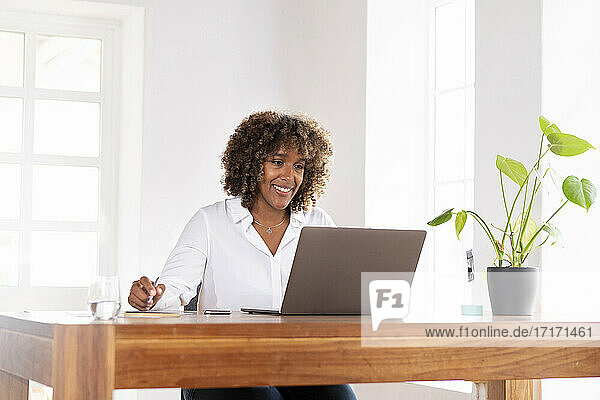 Lächelnde Geschäftsfrau  die im Büro zu Hause an einem Laptop arbeitet