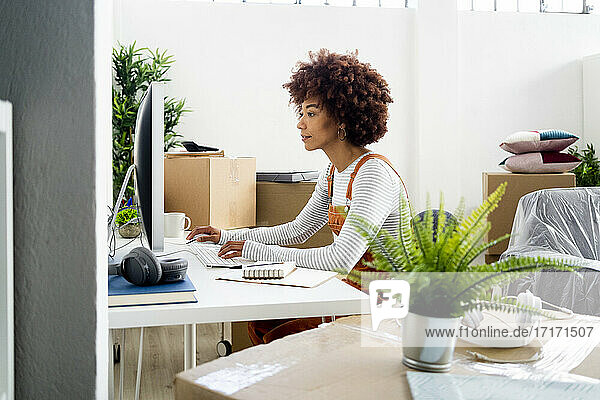 Afro-Frau  die einen Computer benutzt  während sie in ihrer neuen Wohnung von Kartons umgeben ist