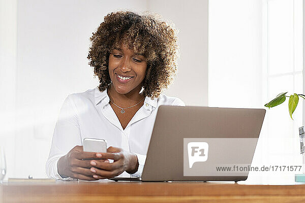 Geschäftsfrau mit Laptop und Mobiltelefon im Home Office sitzend