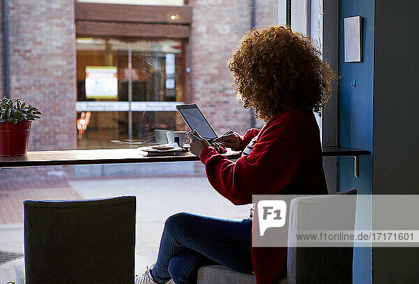 Young woman using digital tablet while sitting at cafe