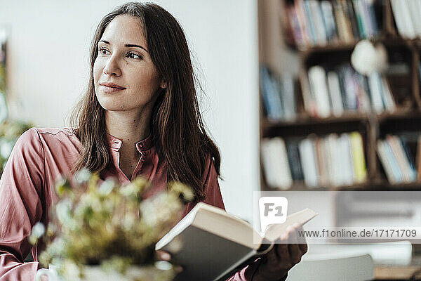 Nachdenkliche Geschäftsfrau mit einem Buch in einem Cafe