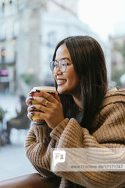 Smiling young woman looking through window while having coffee in cafe