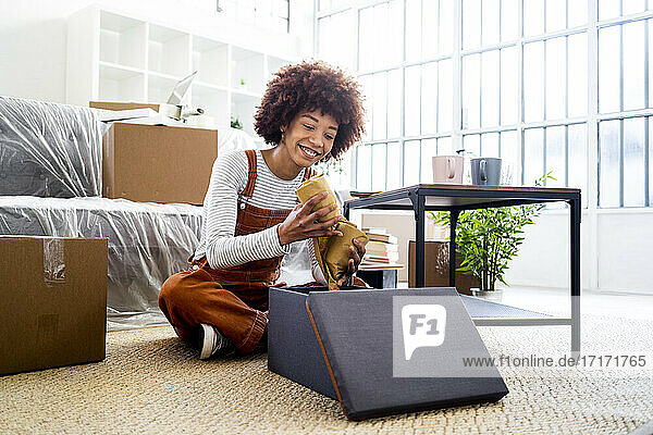 Lächelnde Afro-Frau  die eine eingepackte Brille in einem Karton aufbewahrt  während sie in ein neues Haus zieht