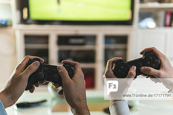 Male friends hands playing video game at home