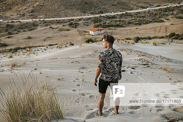 Junger Mann  der wegschaut  während er auf Sand in Almeria  Tabernas-Wüste  Spanien  steht